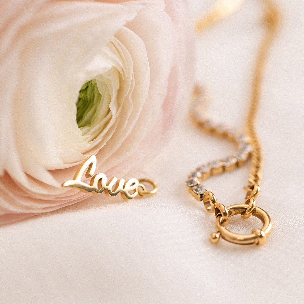 Love Charm Anhänger aus 18K Gold Edelstahl, elegant auf hellem Stoff mit zarter Blüte, PURELEI Signature.