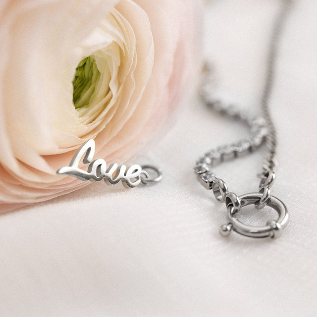 Love Charm aus nickelfreiem Silber mit filigranem Schriftzug, elegant auf weißem Stoff, PURELEI feminine Leichtigkeit