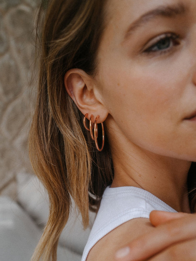Roségoldene Creolen von PURELEI, elegant und modern, getragen am Ohr einer Frau.