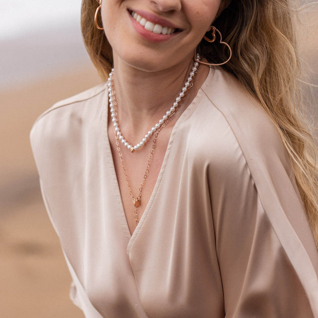 Perlenkette und goldene Anhänger von PURELEI, elegant und feminin, getragen mit sanftem Lächeln.