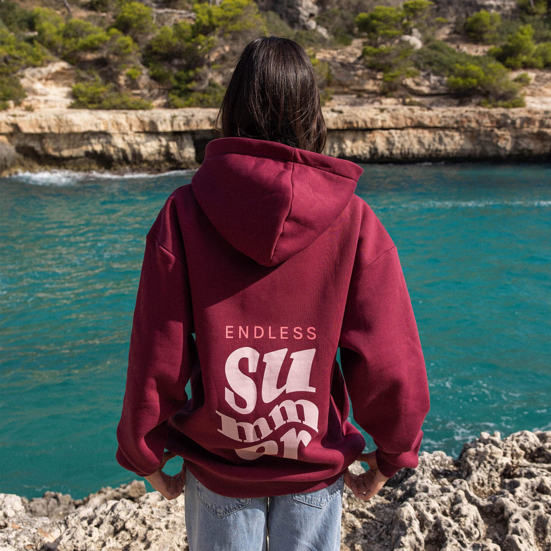 Bordeauxfarbener Hoodie mit Aufdruck ENDLESS SUMMER von PURELEI, lässig am Wasser getragen.