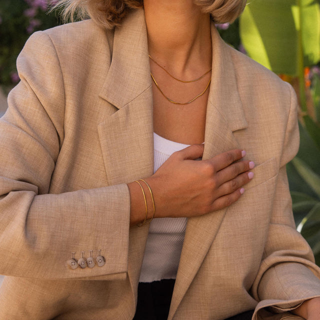 Goldene Ketten und Armbänder von PURELEI, elegant getragen mit beigem Blazer.