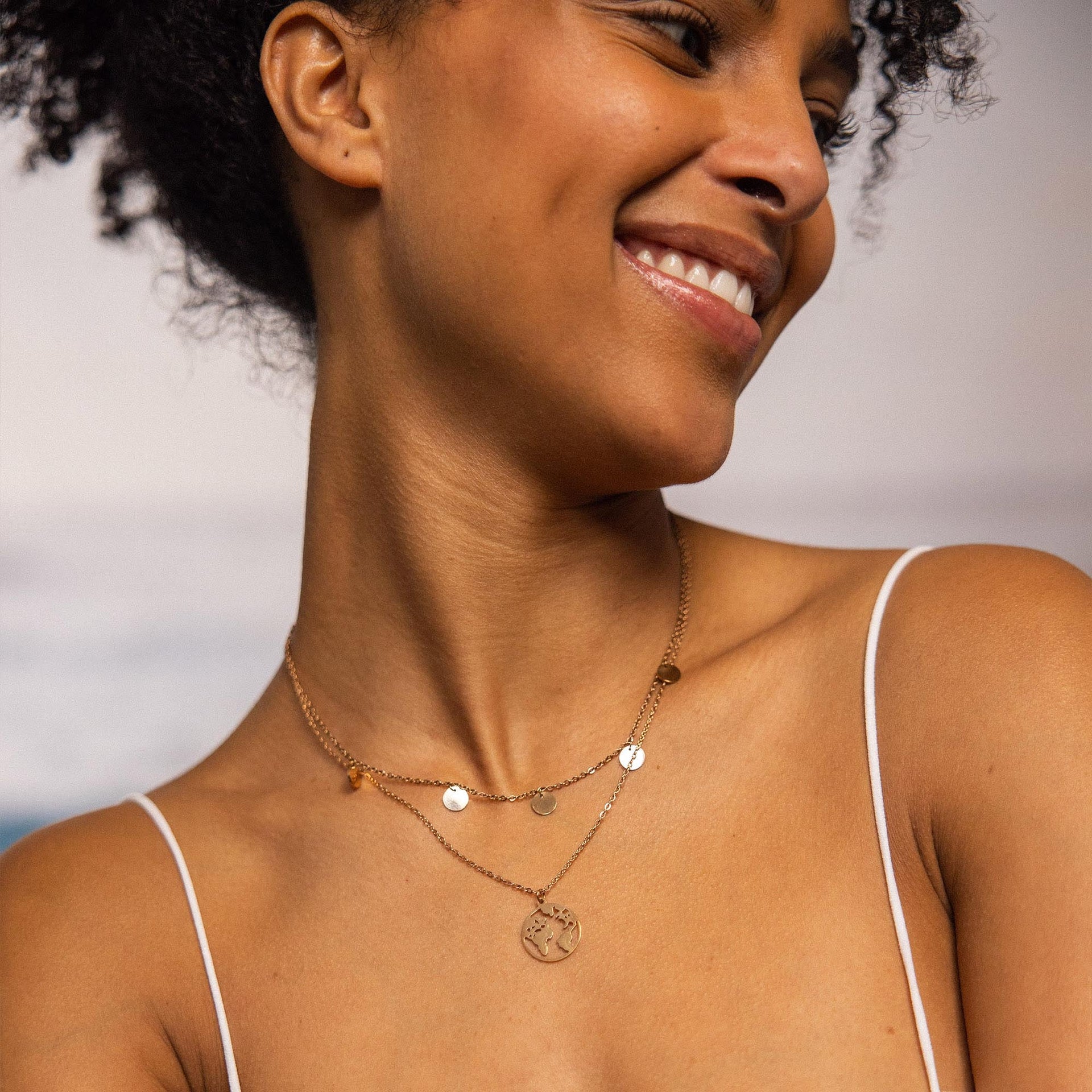 Zarte, goldene Kette mit Anhängern, getragen von einer lächelnden Frau, PURELEI inspiriert.