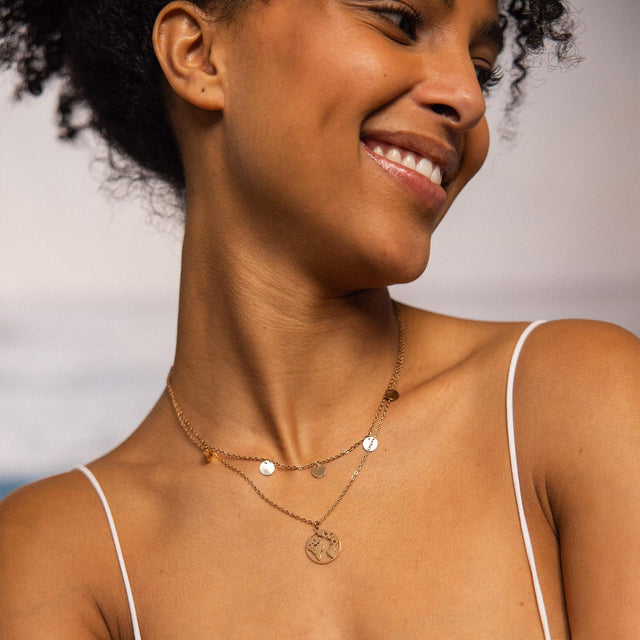 Zarte, goldene Kette mit Anhängern, getragen von einer lächelnden Frau, PURELEI inspiriert.