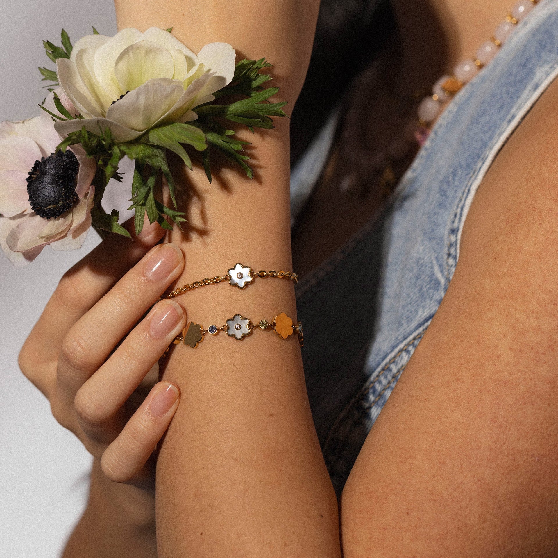 Zartes Armband aus Roségold mit blütenförmigen Anhängern, getragen mit Blumen im Hintergrund – PURELEI.