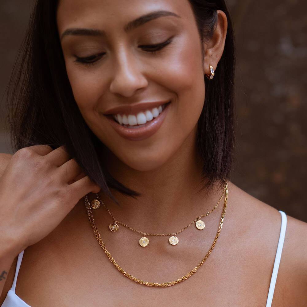 Zarte, roségoldene Kette mit Sonnenmotiv von PURELEI, getragen mit lässigem Outfit.