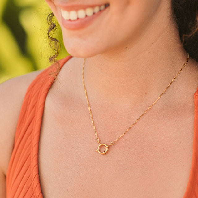 Filigrane, vergoldete Lokahi Charm Kette von PURELEI, leicht gedreht, am Hals mit sommerlicher, natürlicher Stimmung.