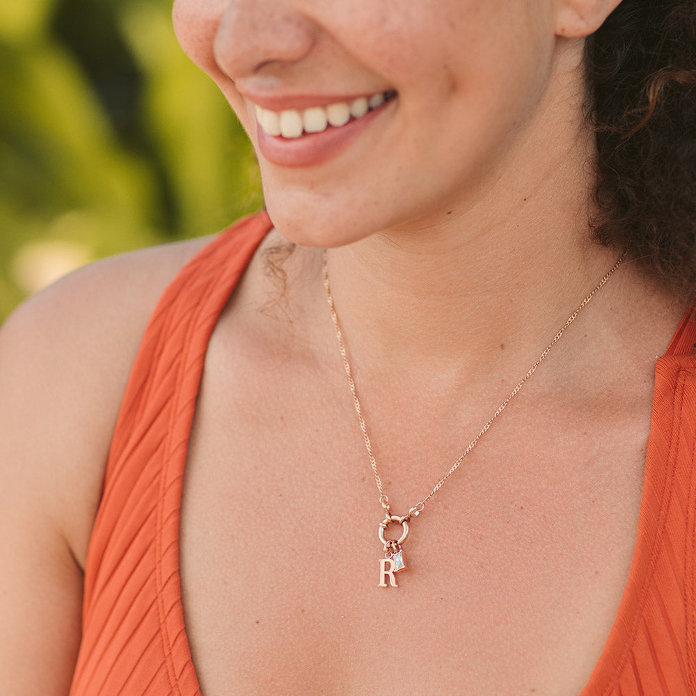 PURELEI Pure R Charm Anhänger aus 18K Roségold vergoldetem Edelstahl, elegant und feminin getragen am Dekolleté.