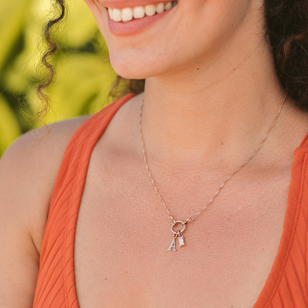 Feine, nickelfreie Lokahi Charm Kette in Roségold mit Buchstabenanhängern, getragen vor grünem Naturhintergrund, PURELEI.