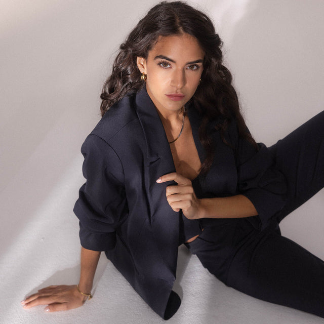 Elegante Frau in dunklem Blazer, PURELEI Schmuck funkelt im sanften Licht.