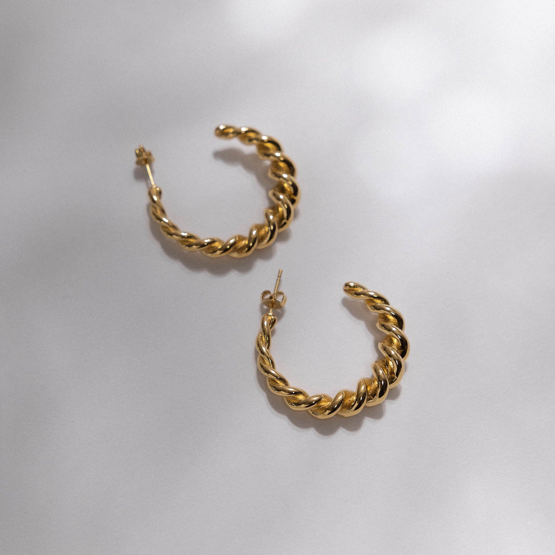 Goldene, gedrehte Creolen von PURELEI auf hellem Hintergrund, elegant und feminin.