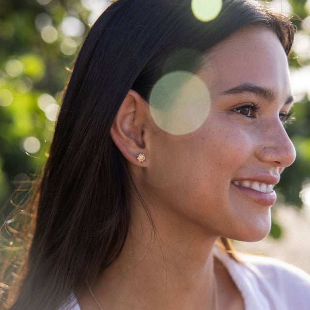 Goldene Ohrringe mit Sonnenmotiv, getragen von einer lächelnden Frau im Freien – PURELEI.