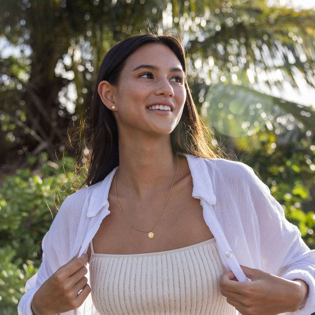 Goldene PURELEI Kette mit Sonnenmotiv, getragen in tropischer Umgebung.