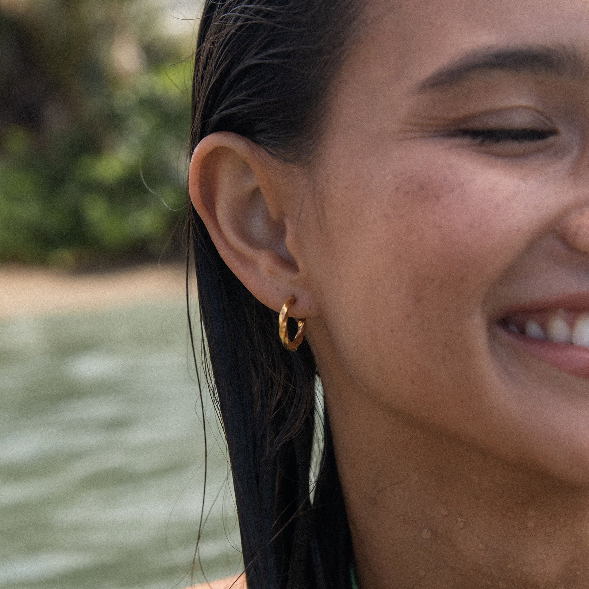 PURELEI Kelani Ohrringe Gold-Creolen mit gewundenem Design, getragen am Strand – warm, elegant und nickelfrei.