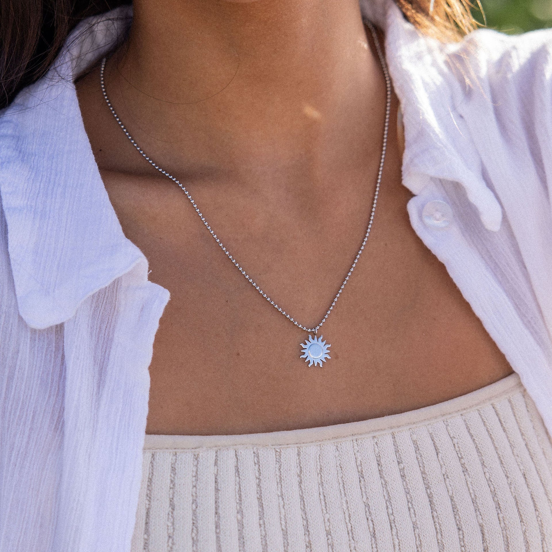 Silberne Sonnensonnenkette von PURELEI, elegant und strahlend, getragen auf Haut mit weißem Oberteil.