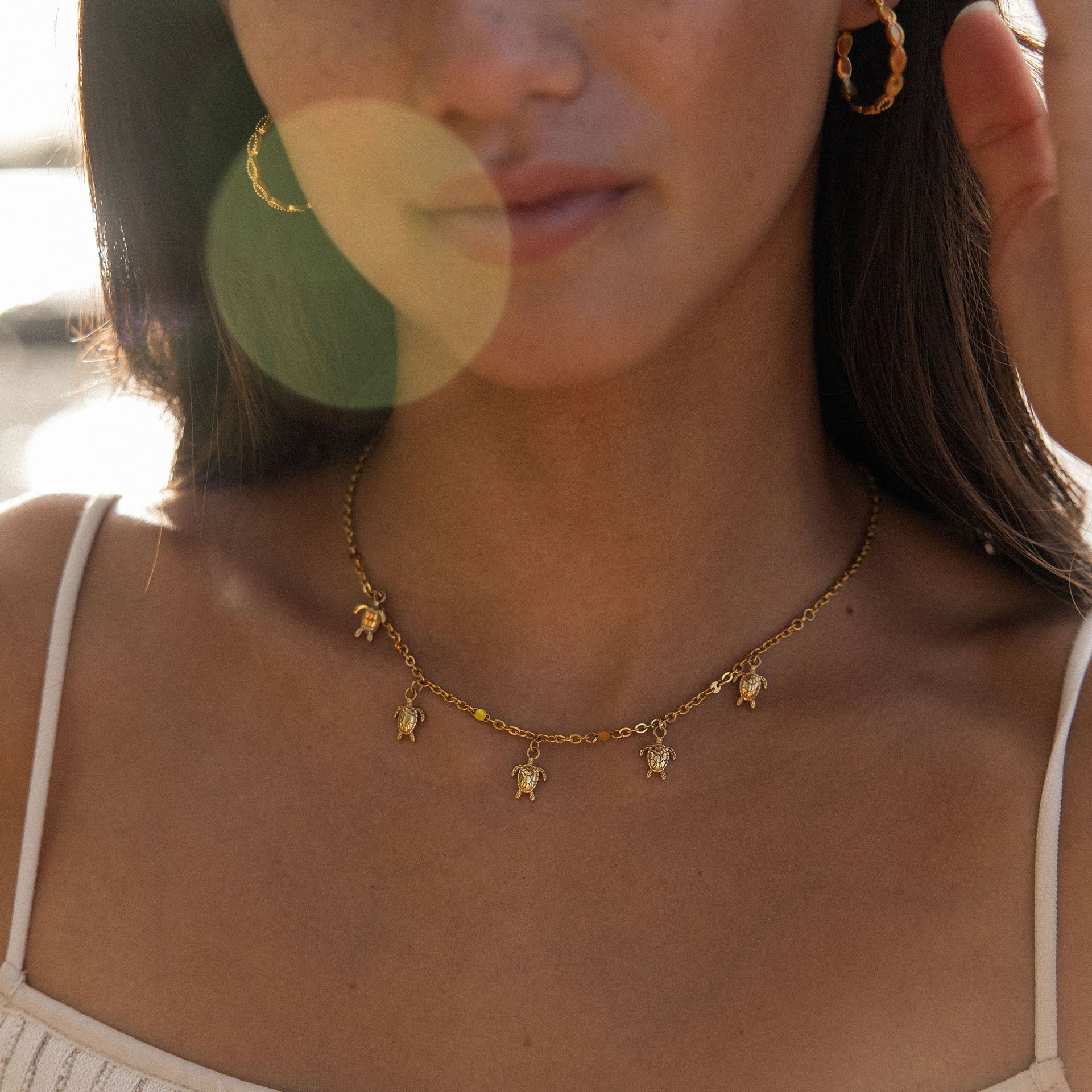 Goldene Kette mit Schildkröten-Anhängern, getragen in warmem Licht, von PURELEI.