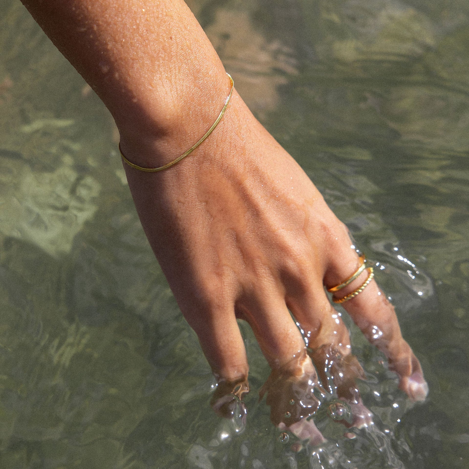 PURELEI Kanani Armband aus 18K Gold, zart gewölbt, am Handgelenk im Wasser getragen, elegant und zeitlos.