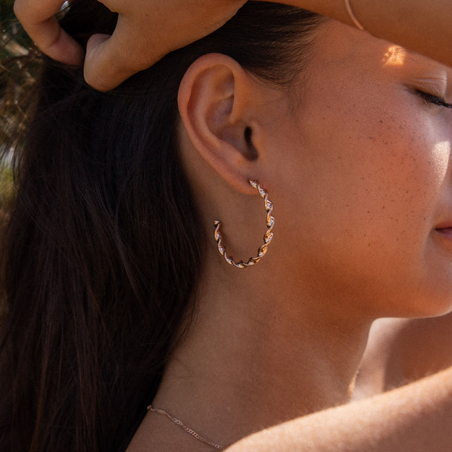 PURELEI Kaula Creole Ohrringe in Roségold mit gedrehtem Design, getragen bei warmem Sonnenlicht am Ohr.