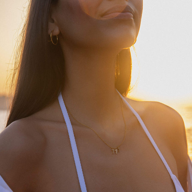 Goldene 777 Kette mit Zirkonia an filigraner Ankerkette, getragen im warmen Sonnenlicht, PURELEI 