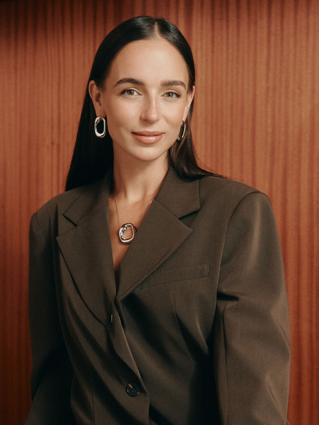 Elegante PURELEI Ohrringe und Kette in Gold, getragen mit einem modernen Blazer.