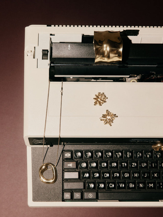 Silberne Kette mit organischem Anhänger auf einer Schreibmaschine, PURELEI inspiriert.