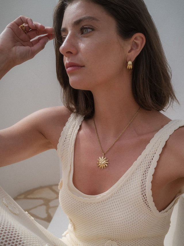 Goldener Iconic Sun Charm aus Edelstahl, getragen zu warmem Licht, elegant und feminin – PURELEI Schmuck mit Insel-Spirit.