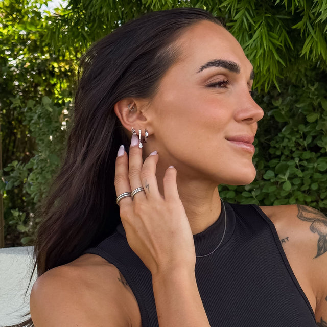 Silberne Creolen und Ringe von PURELEI, elegant und modern, umgeben von grünem Hintergrund.