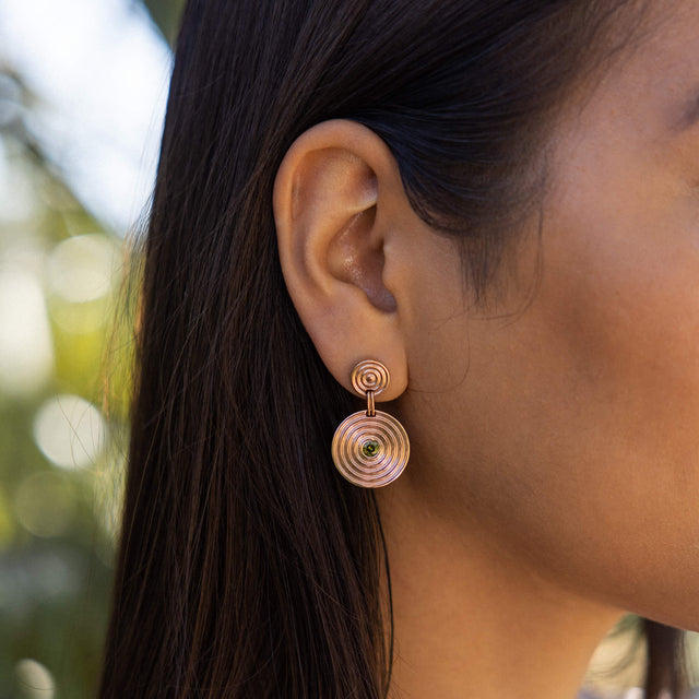 Artistic Ohrringe aus roségoldenem Edelstahl mit zwei Ringen und grün funkelndem Zierstein, elegant am Ohr.