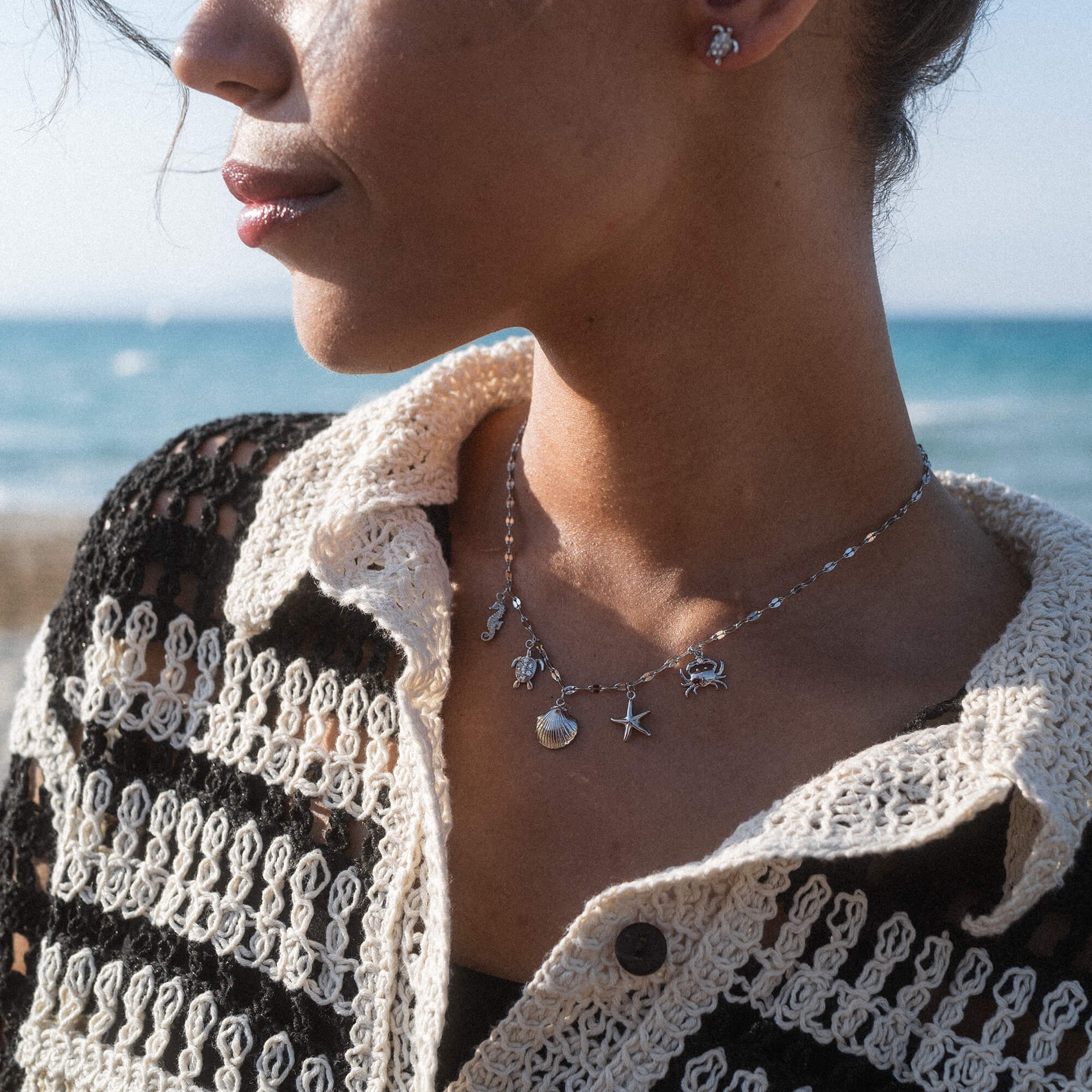 Silberne Kette mit maritimen Anhängern, getragen am Strand, von PURELEI.