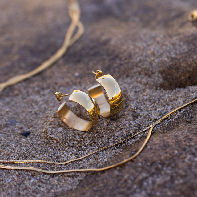 Glänzende PURELEI Glowing Ohrringe in 18K Gold mit breitem Design auf warmem Sand – elegant und zeitlos.