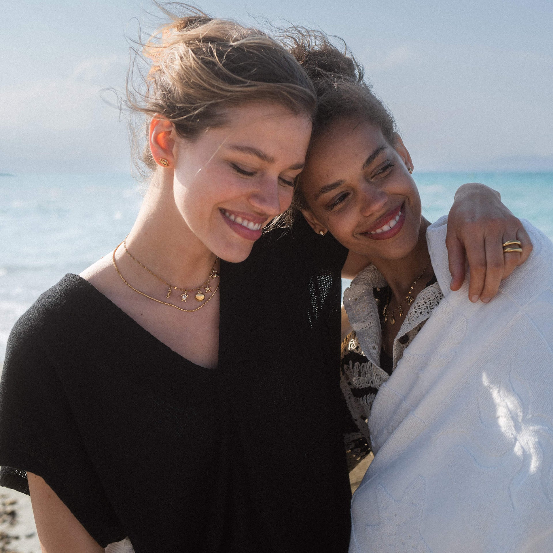 Zwei Frauen am Strand, eine trägt eine zarte PURELEI Kette mit Muschelanhänger, warmes Licht.