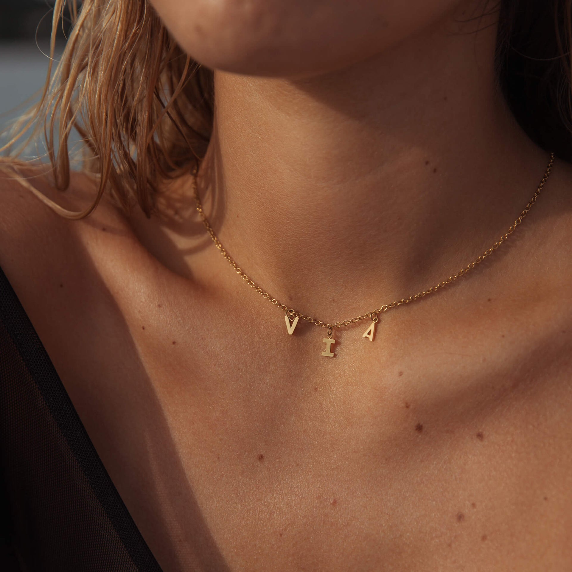 Goldene Buchstabenkette von PURELEI, elegant und feminin, getragen auf nackter Haut.