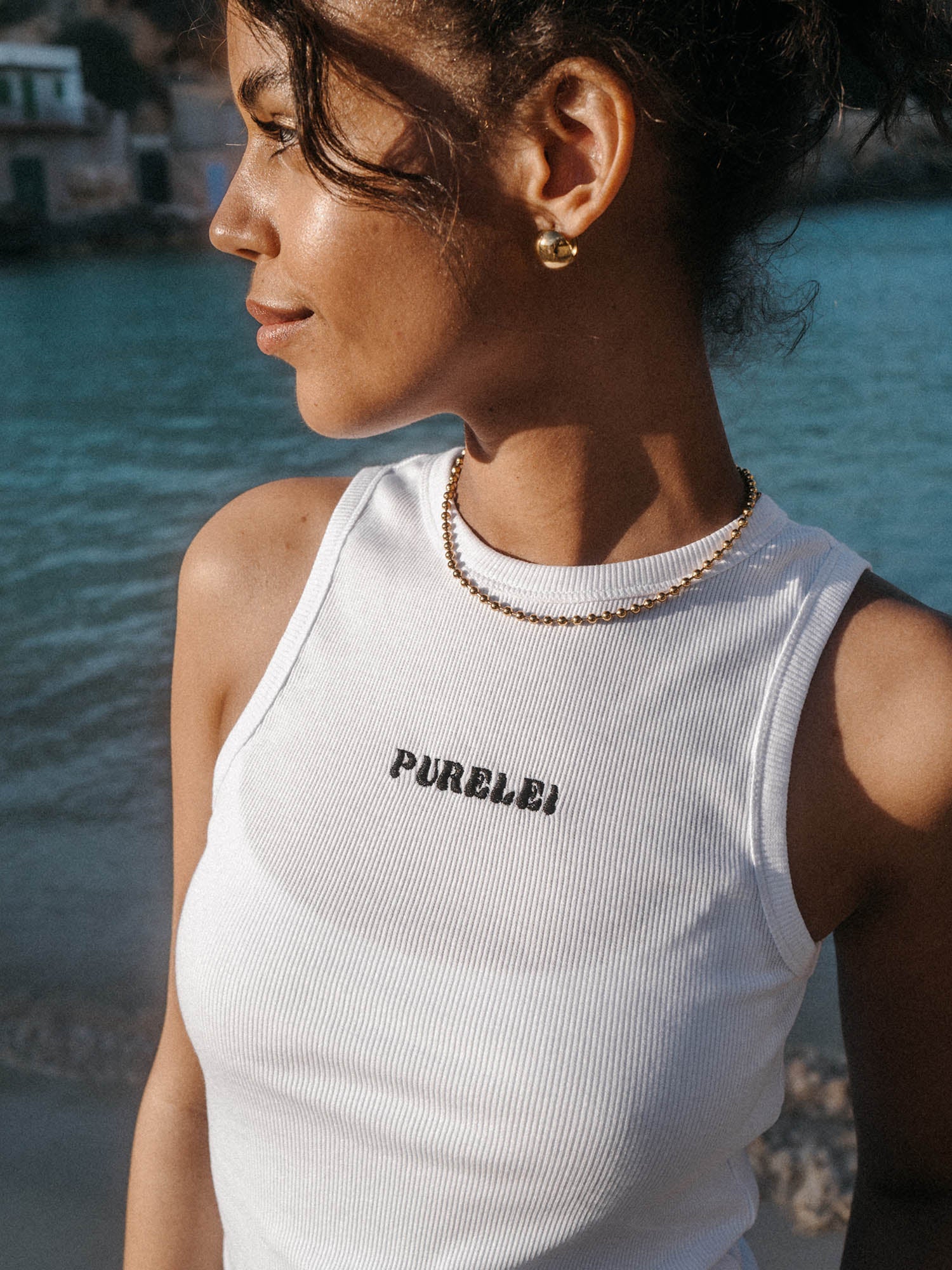 Feminines, weißes Oberteil mit PURELEI-Logo, getragen am Strand, strahlende Stimmung.