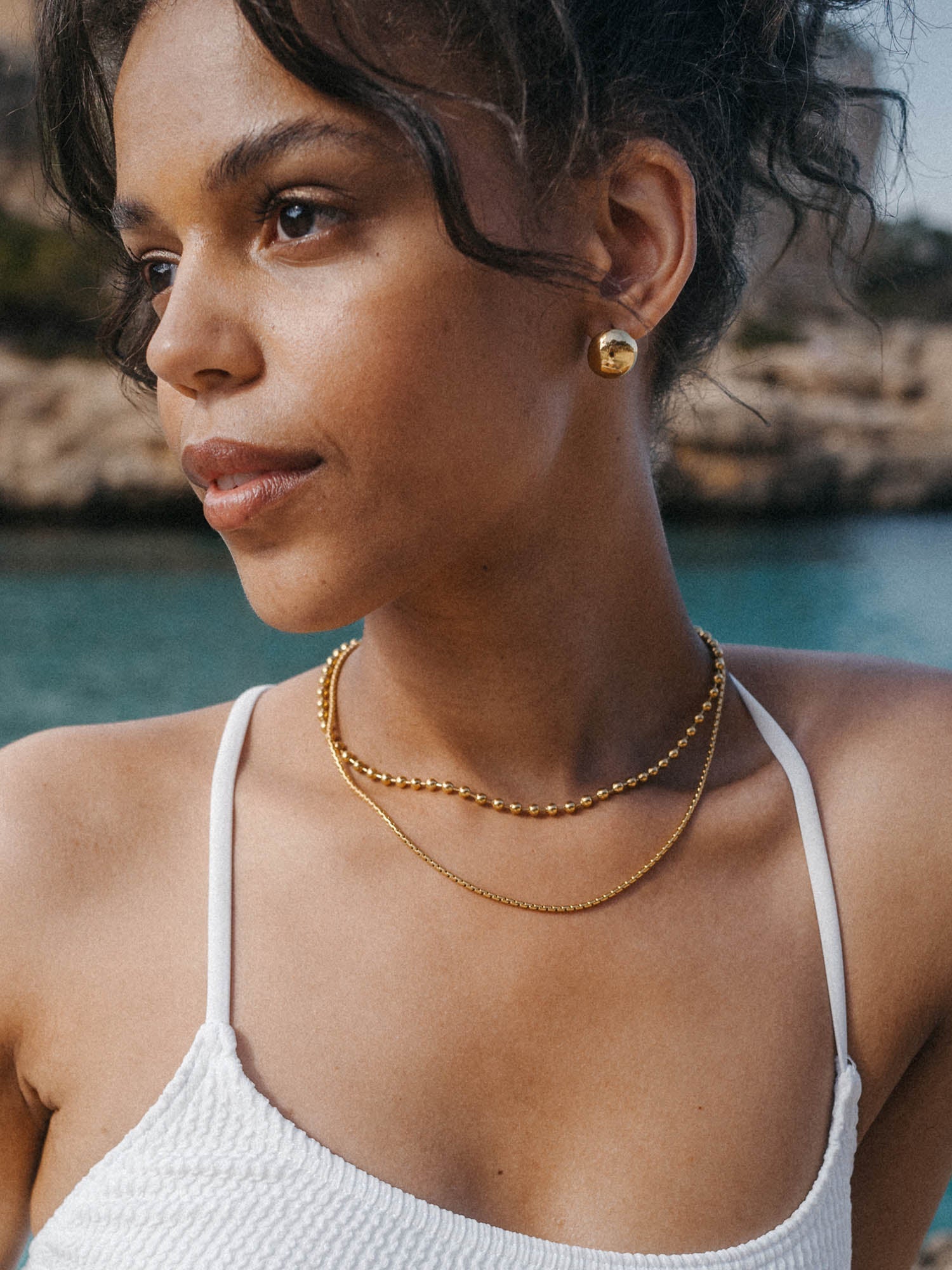 Zarte roségoldene Ketten und Ohrringe von PURELEI, elegant und feminin am Strand getragen.