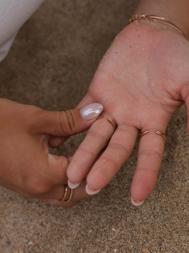 Roségoldene Ringe auf einer Hand, umgeben von Sand, PURELEI inspiriert.