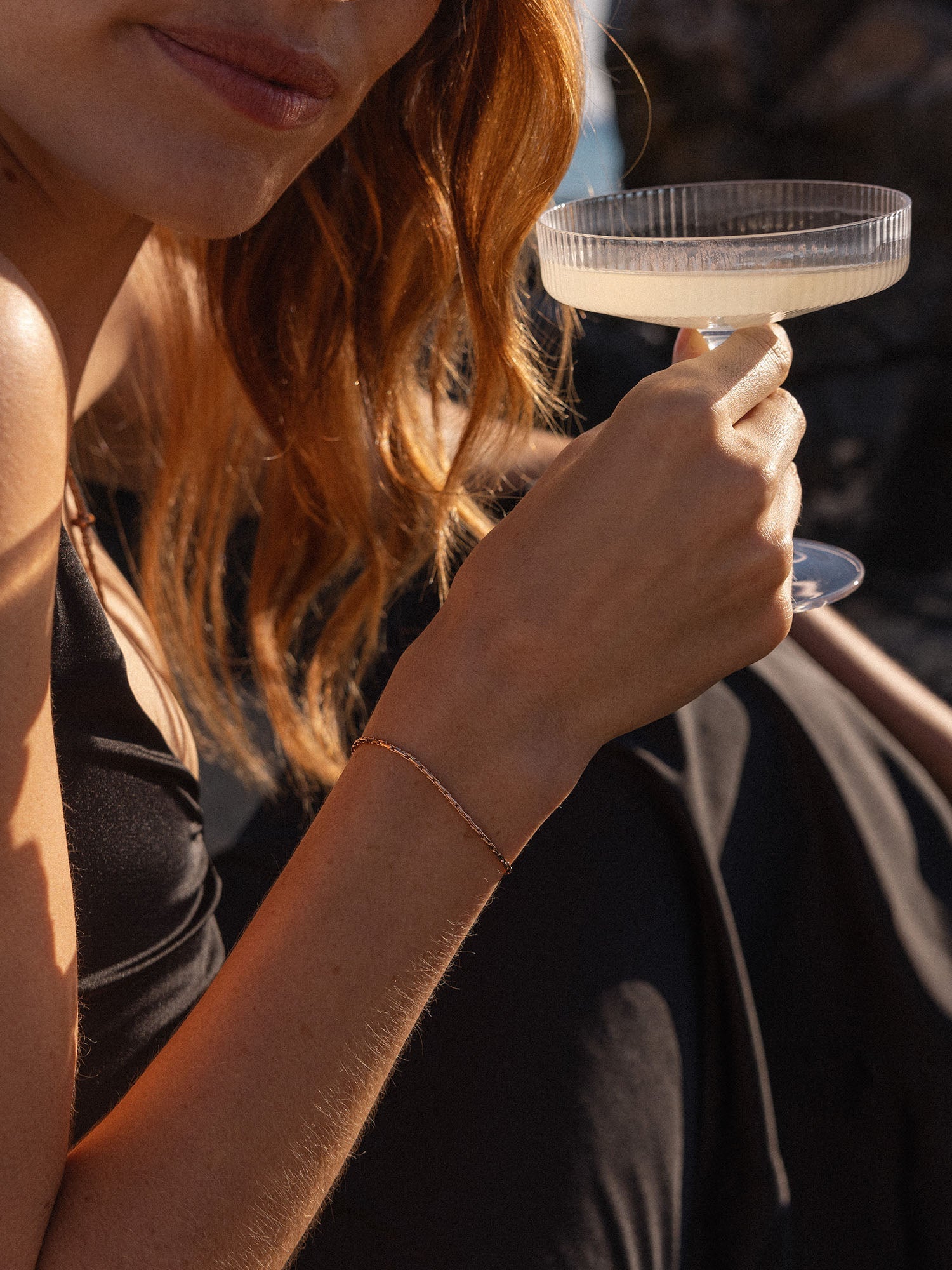 Goldenes Armband von PURELEI, elegant und feminin, getragen mit einem Cocktailglas.