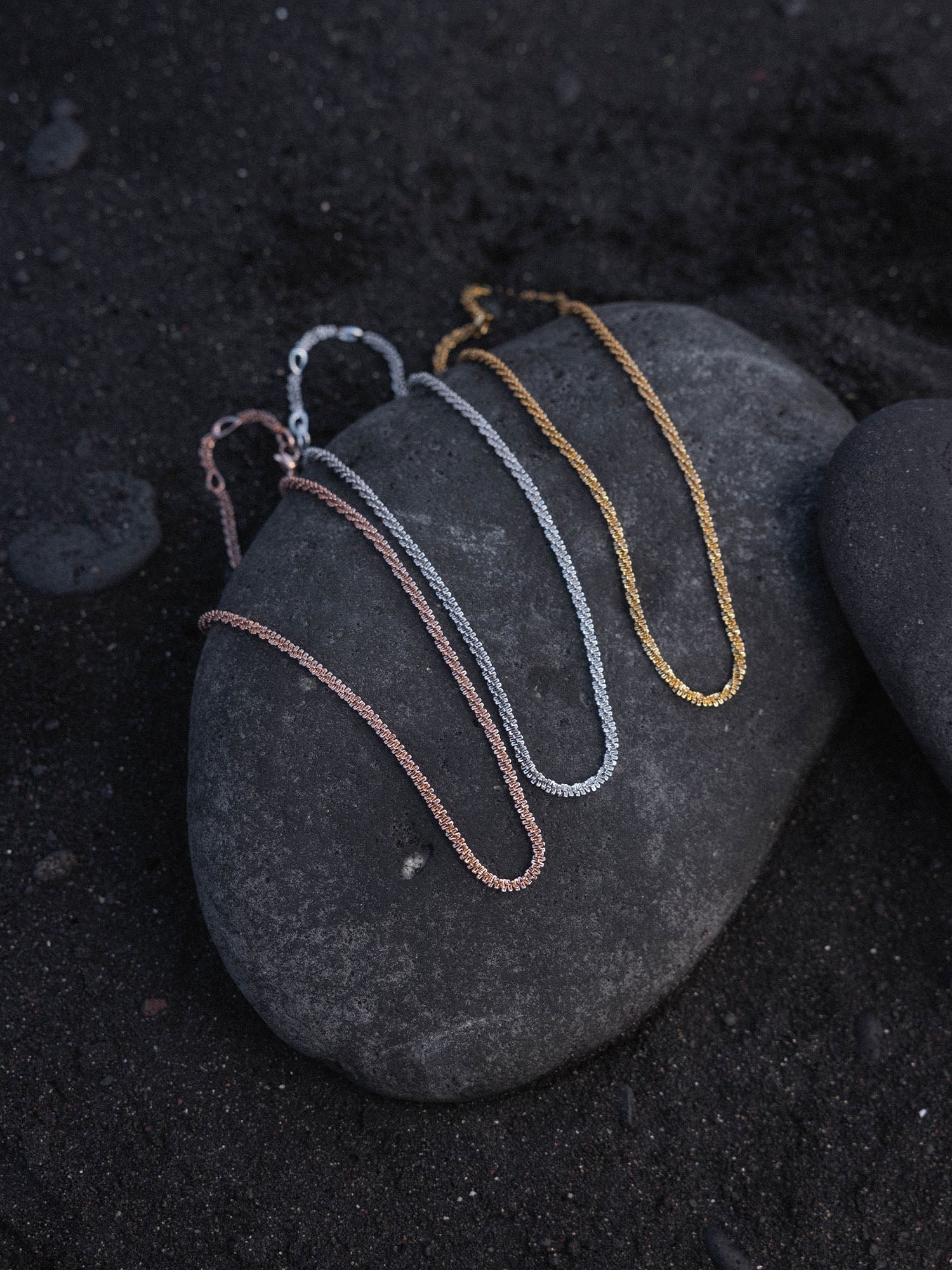 Dreifache PURELEI Lava Kette in Gold, Silber und Roségold mit gedrehter Struktur auf dunklem Lavastein.