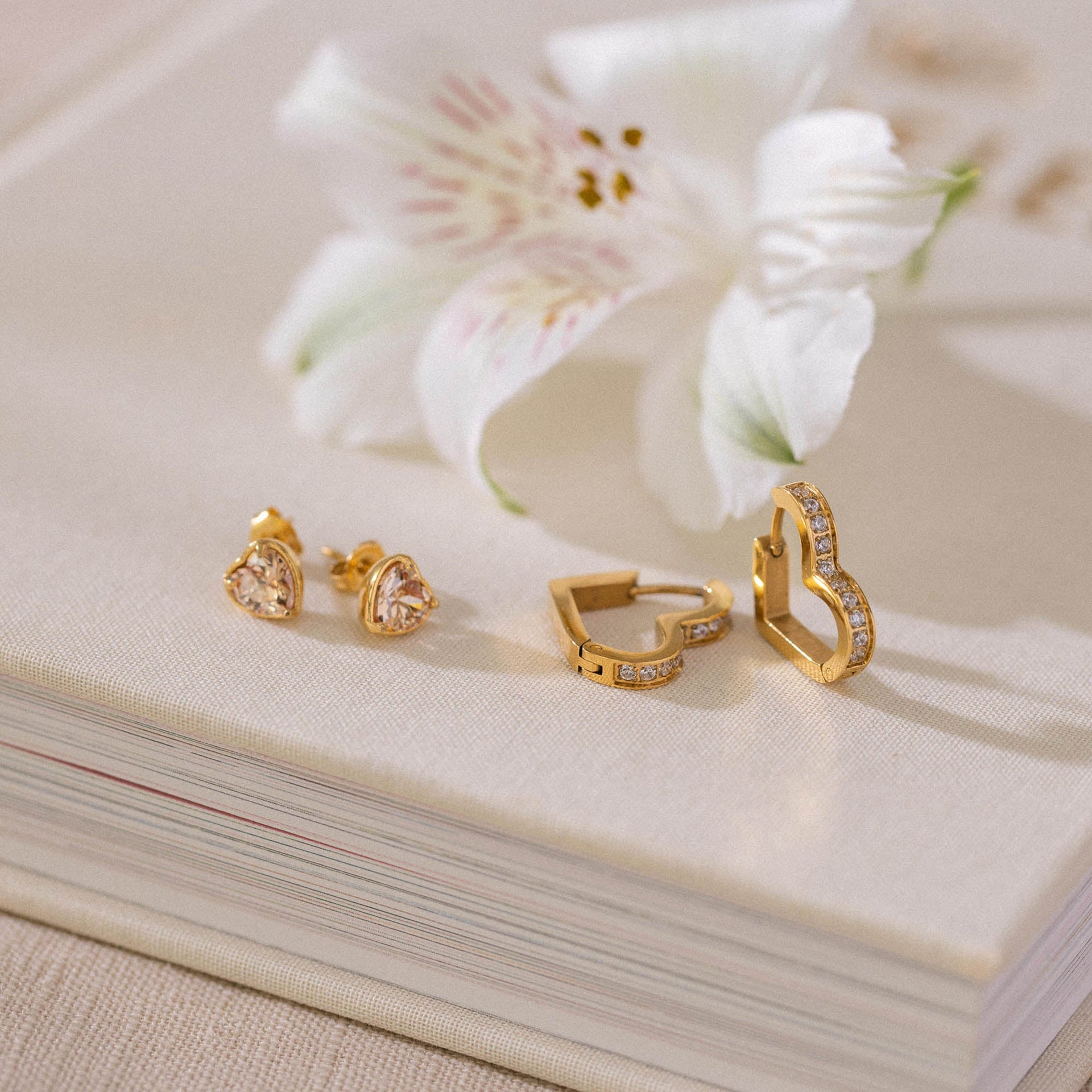 Zarte goldene Ohrringe mit funkelnden Details, inspiriert von PURELEI, auf einem Leinenstoff.