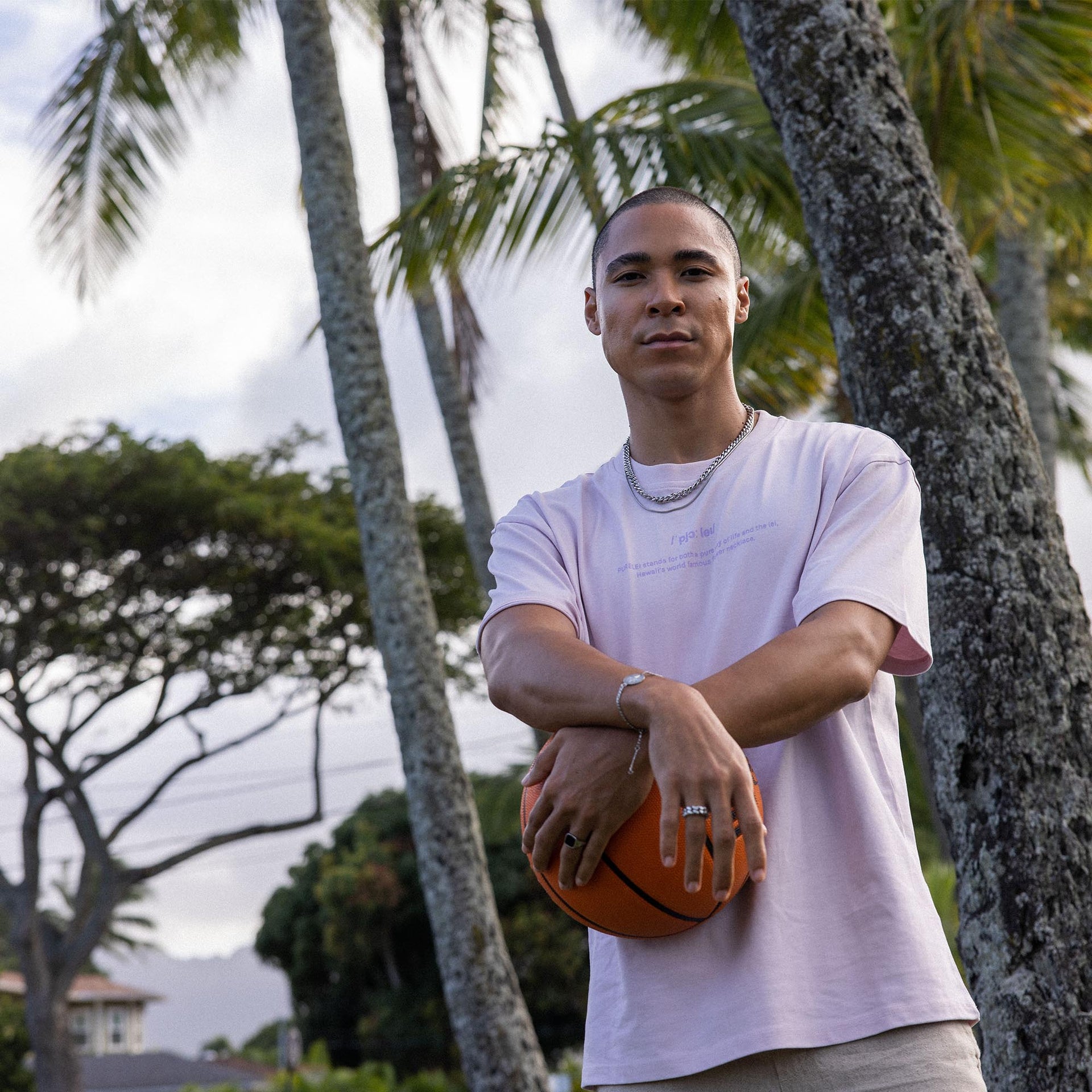Mann mit Basketball, getragen mit PURELEI Schmuck, umgeben von Palmen im Freien.