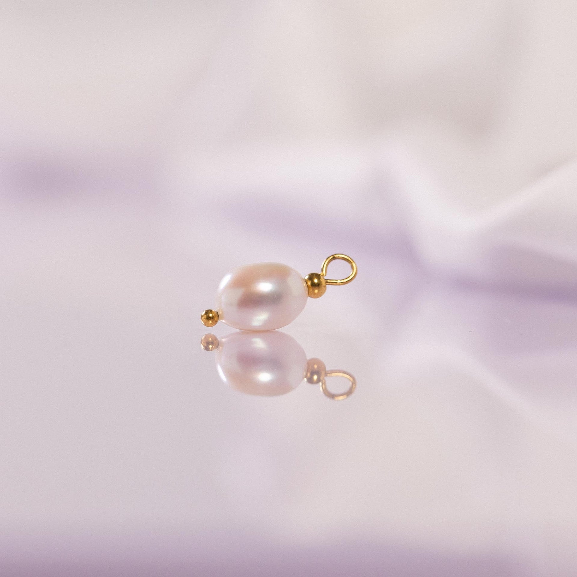 Perlenanhänger von PURELEI, elegant in sanften Rosatönen, auf spiegelndem Untergrund.