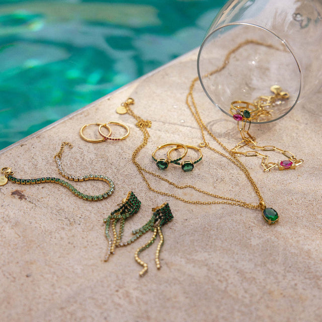 Vielseitiger Schmuck von PURELEI: Goldene Ohrringe und Ketten auf hellem Untergrund, umgeben von Wasser.