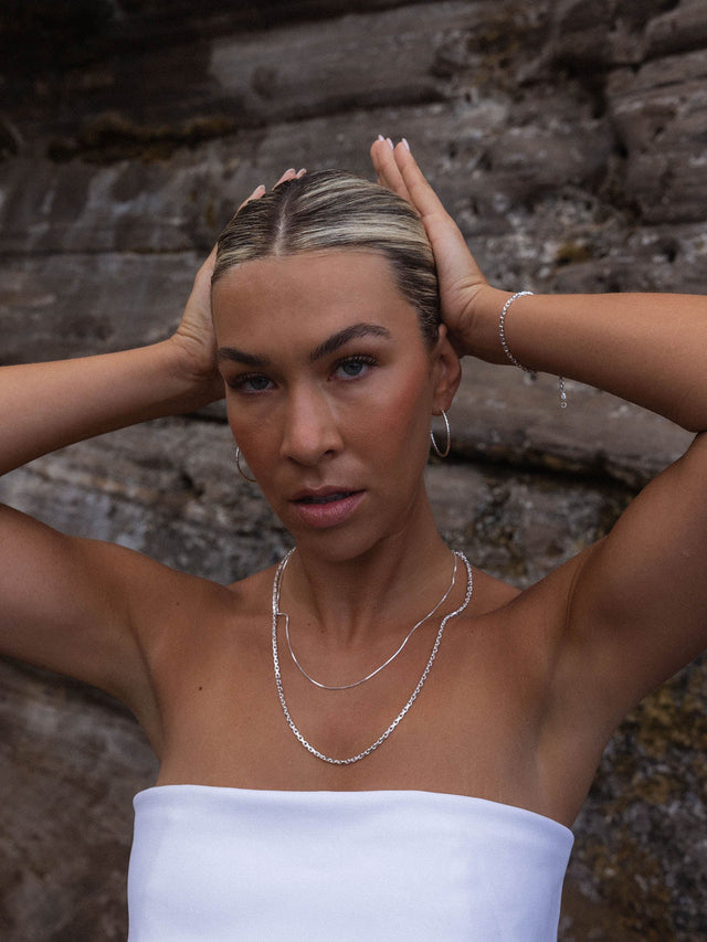 PURELEI Gleam Ohrringe aus facettiertem Silber, elegant und zeitlos, getragen vor natürlichem Fels-Hintergrund