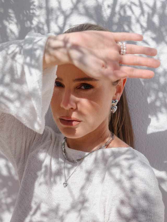 Silberne Ohrringe und Kette von PURELEI, elegant im Sonnenlicht mit Schattenmustern.