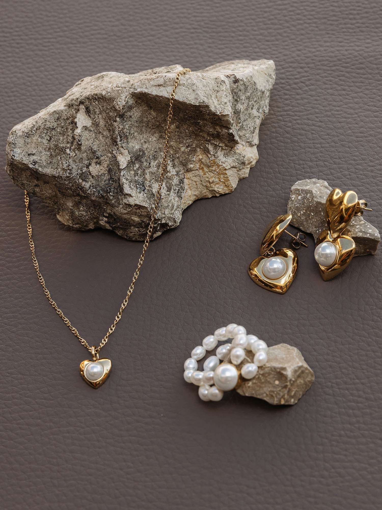 Silberne Herz-Kette und Ohrringe mit Perlen, PURELEI, auf grauem Stein präsentiert.