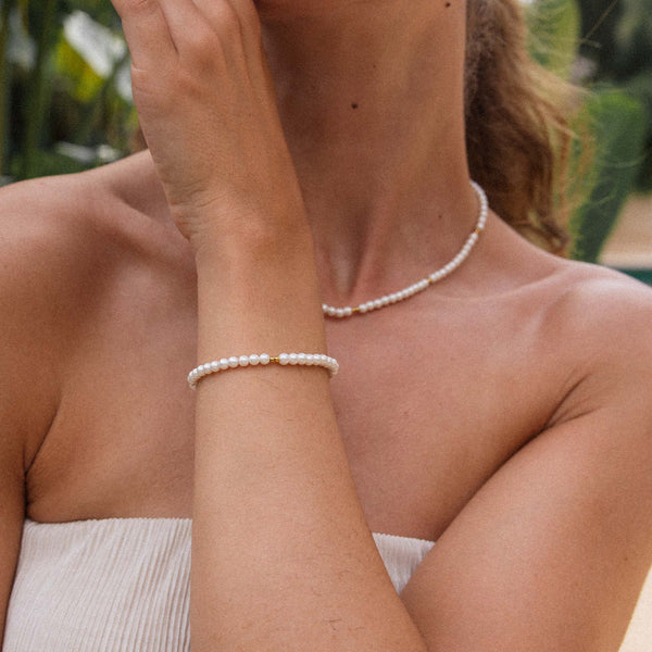 Weiße Perlenkette und Armband von PURELEI, elegant und feminin, umgeben von tropischer Atmosphäre.