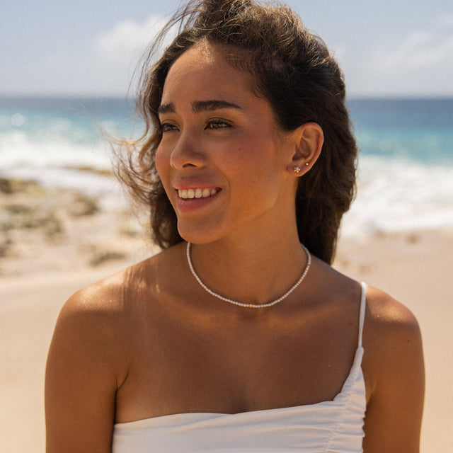 Zarte, allergenfreundliche Perlenkette von PURELEI, getragen am Strand mit tropischer Stimmung.