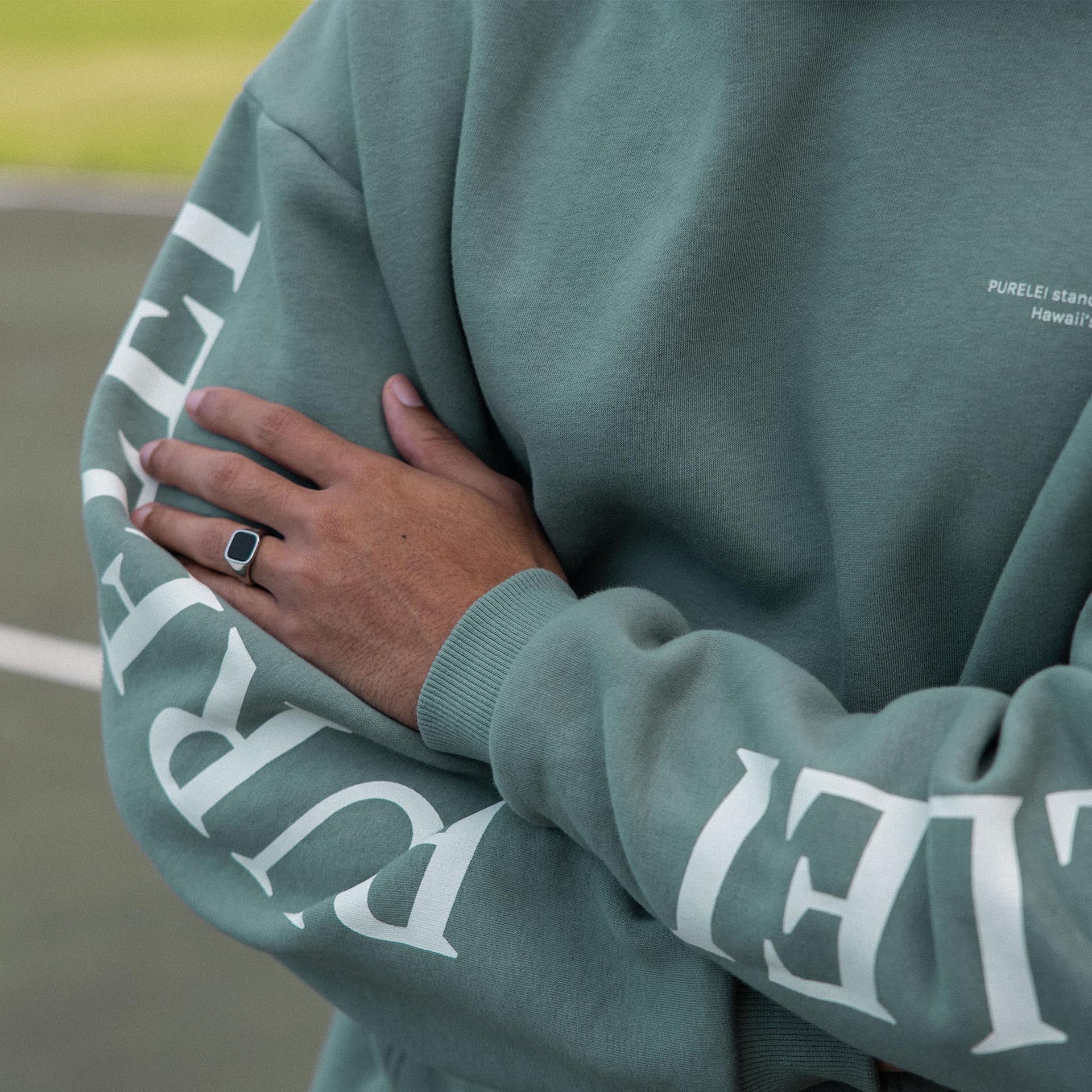 Locker sitzender PURELEI Wave Hoodie in Salbei mit weißem Schriftzug auf Armen und Brust, nachhaltig und bequem.