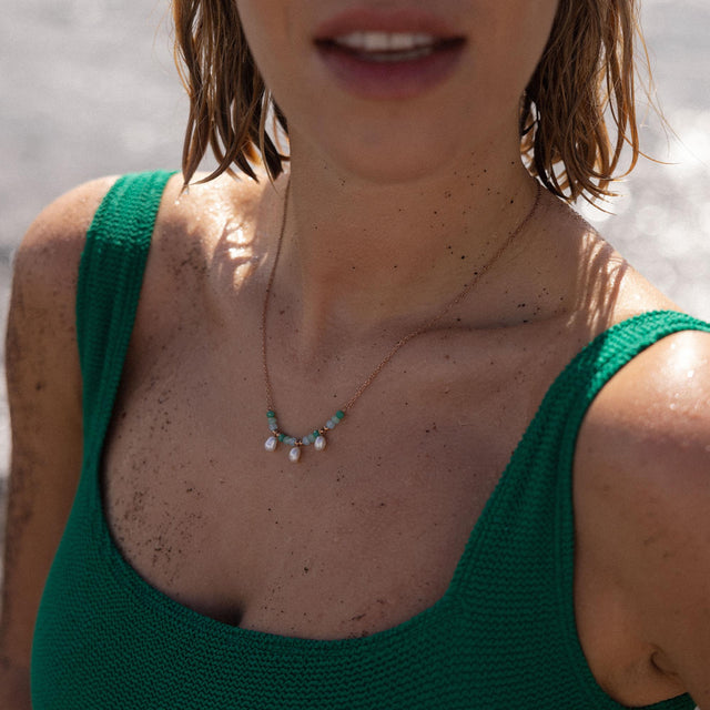 Zarte goldene Kette mit Muschel- und grünen Steinen, getragen am Strand – PURELEI.