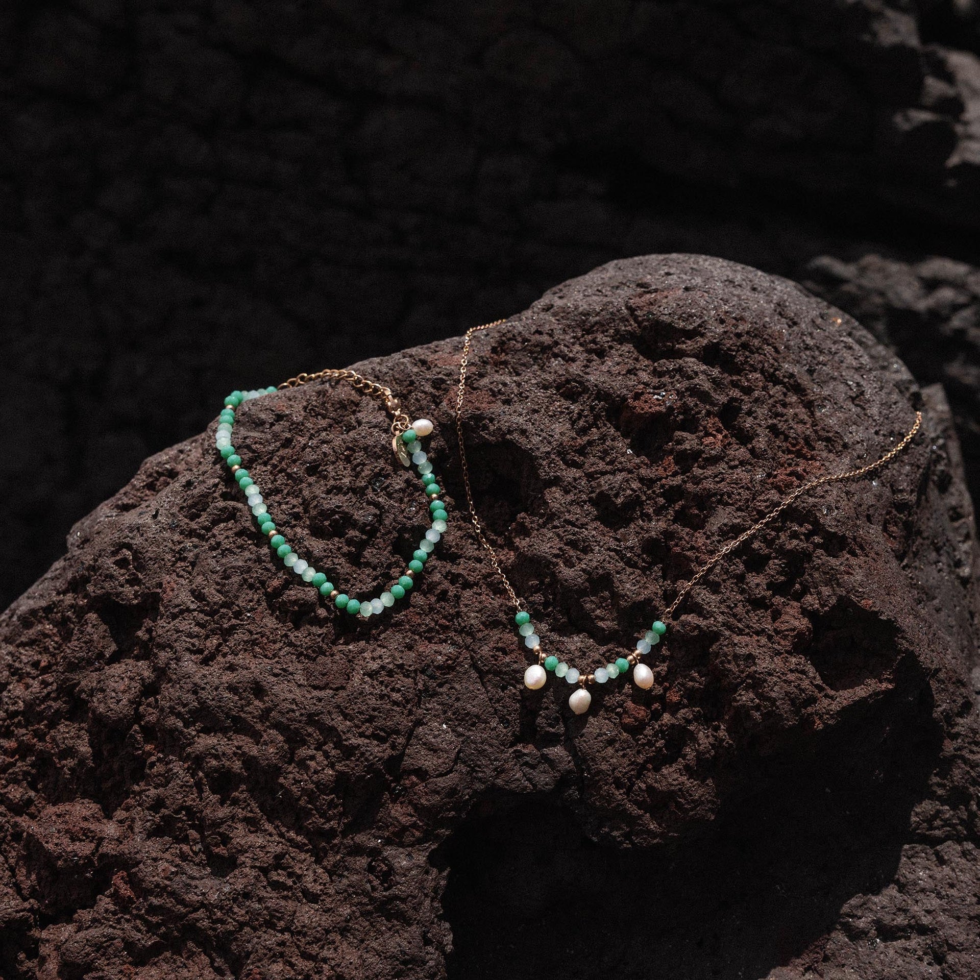 Zwei zarte Ketten mit weißen Perlen auf dunklem Lavagestein, PURELEI inspiriert.