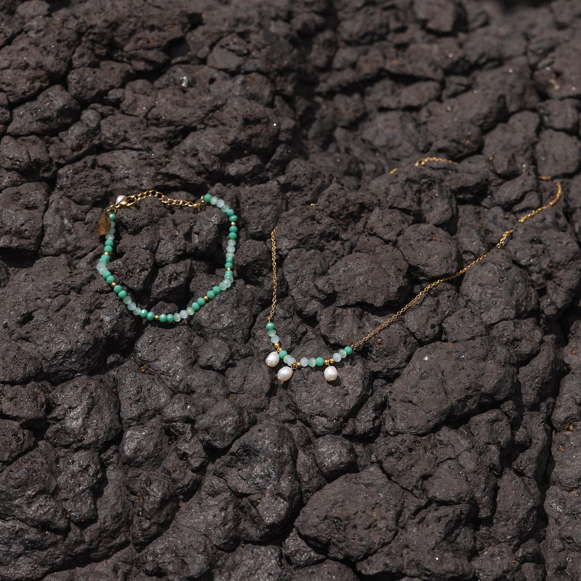 Zarte PURELEI Kette und Armband aus weißen Perlen auf dunklem Lavagestein.